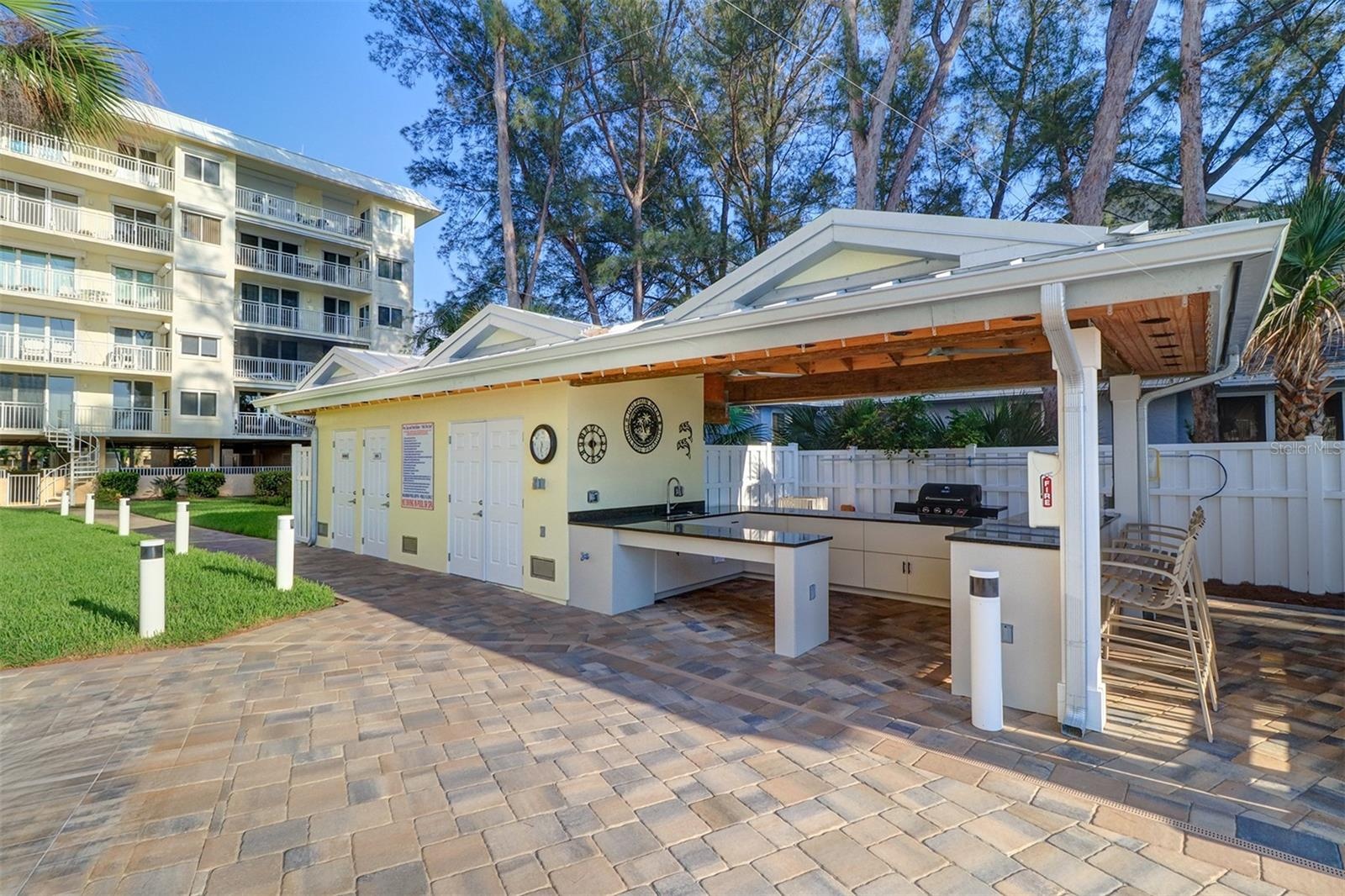 Covered outdoor kitchen with grill, sink and granite bar and countertop prep space, with his & hers pool bathrooms.