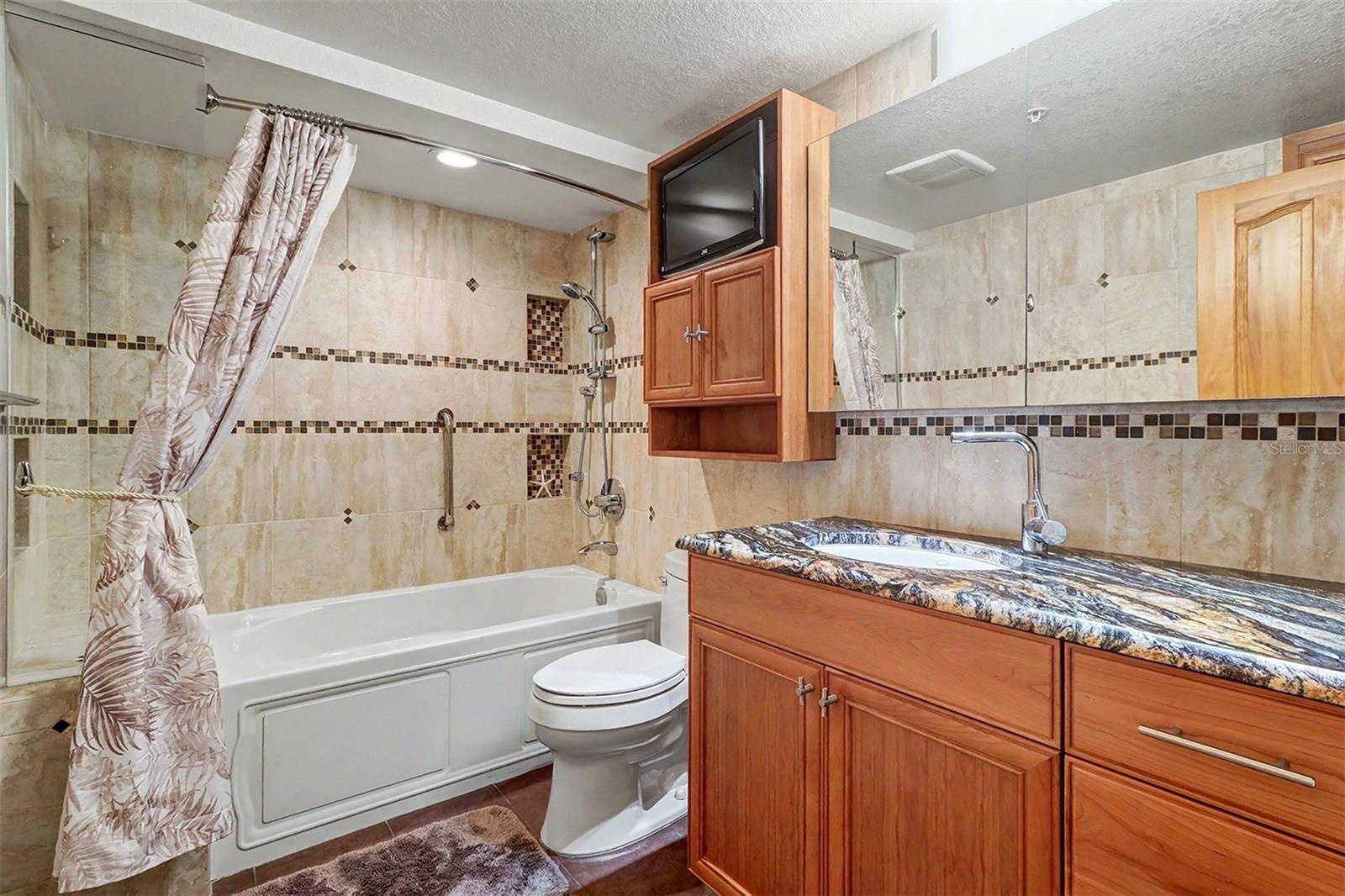 Bathtub- shower combo and a tastefully built in TV enhances the fully tiled guest bathroom.