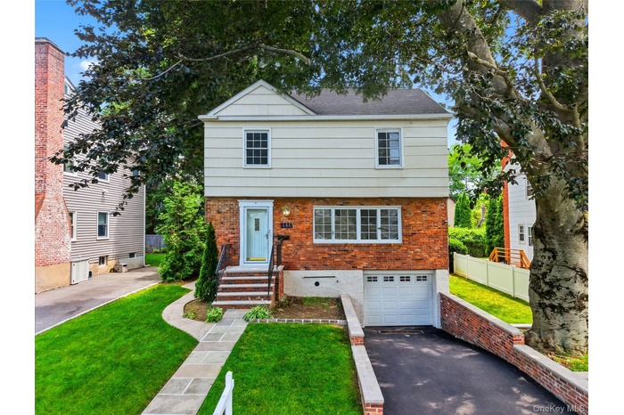 Brick and siding exterior featuring a light blue front door, an integrated garage, a stone walkway, a paved driveway, and established landscaping