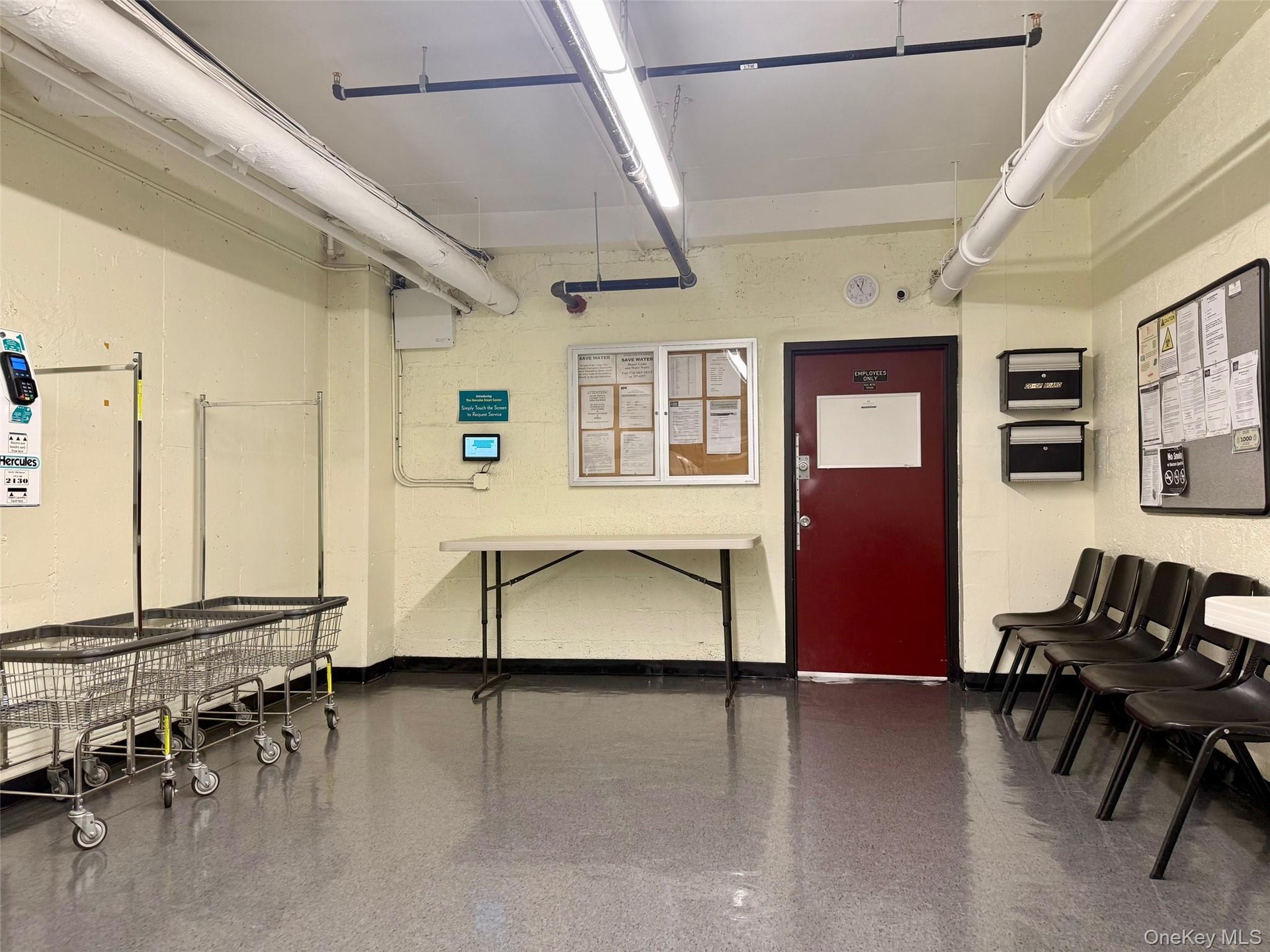 Community laundry room featuring multiple front-loading washing machines, durable flooring, and overhead fluorescent lighting