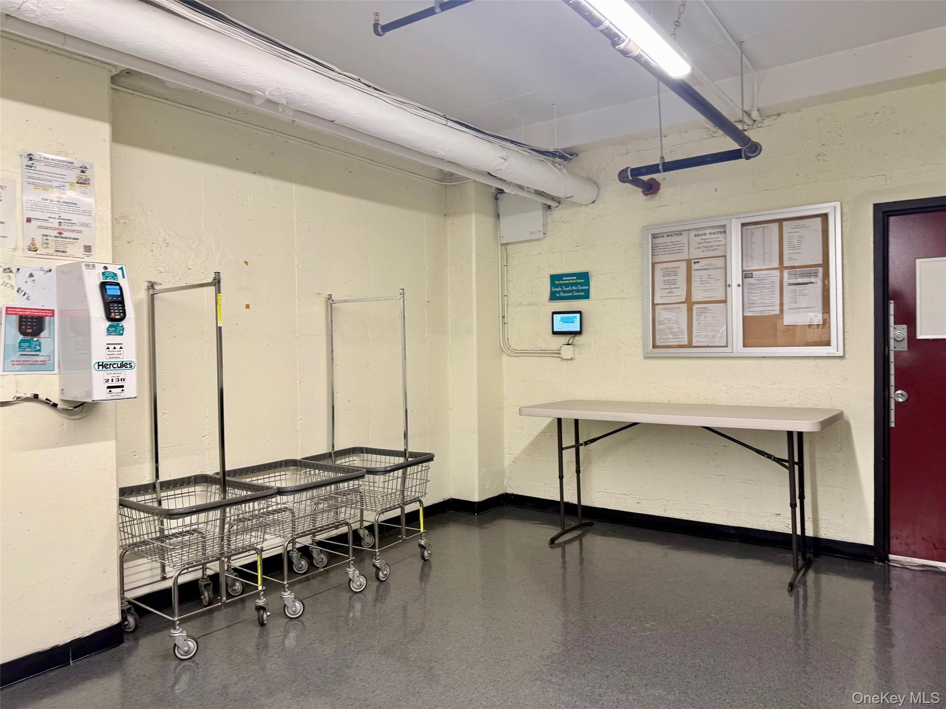 Community laundry room featuring multiple front-loading washing machines, durable flooring, and overhead fluorescent lighting