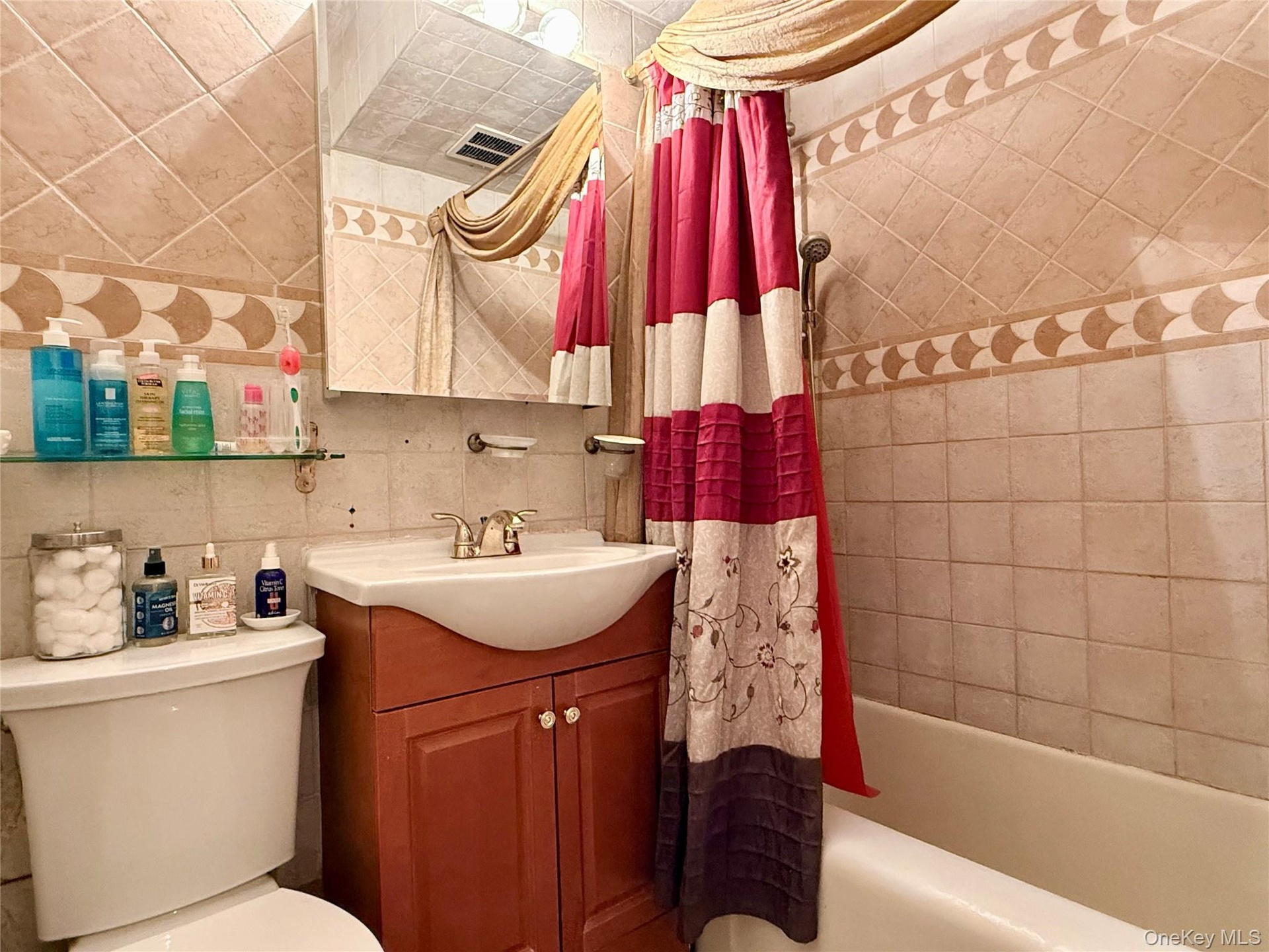 Bathroom featuring a tiled shower surround with decorative accent banding, a wood-finish vanity with an integrated sink, a wall-mounted mirror, and a 