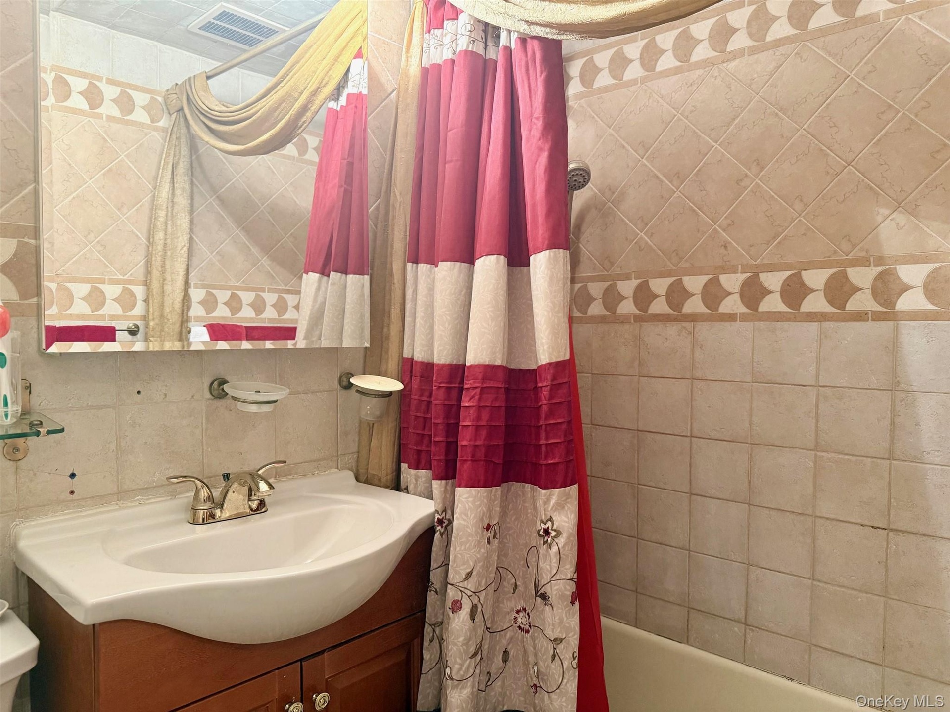 Bathroom featuring a tiled shower surround with decorative accent banding, a wood-finish vanity with an integrated sink, a wall-mounted mirror, and a 