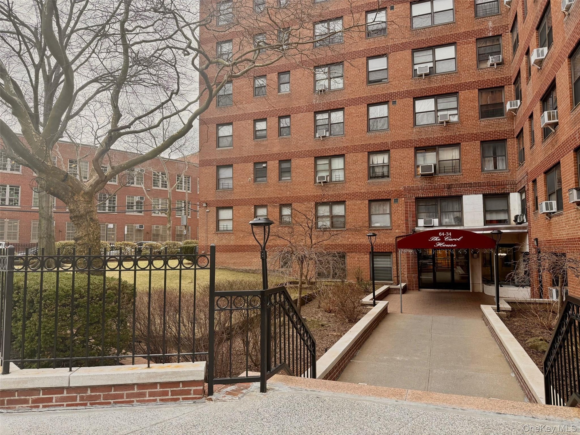 Brick facade building featuring multiple window styles, a covered main entrance, and decorative wrought iron fencing