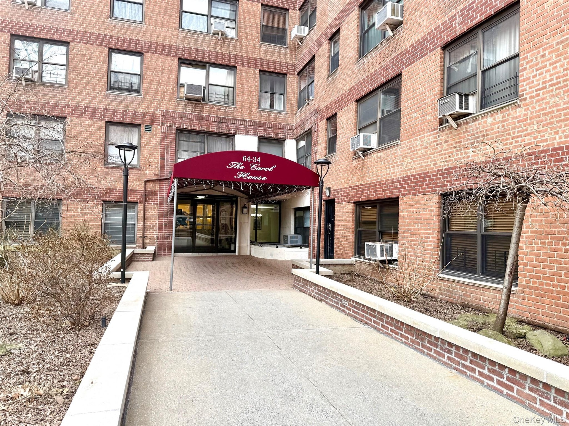 Brick facade building featuring multiple window styles, a covered main entrance, and decorative wrought iron fencing