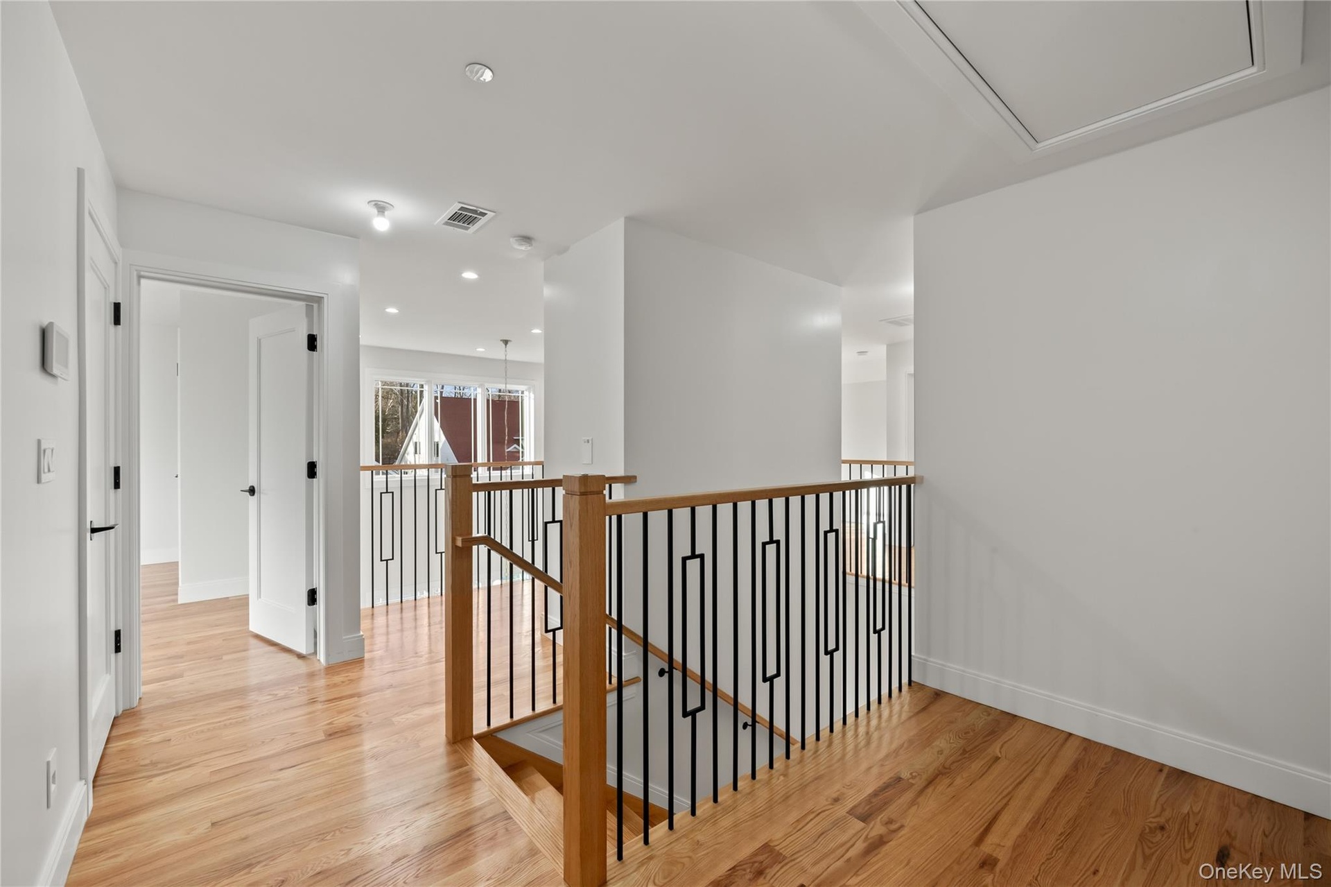 Corridor with an upstairs landing, light wood-style flooring, and recessed lighting