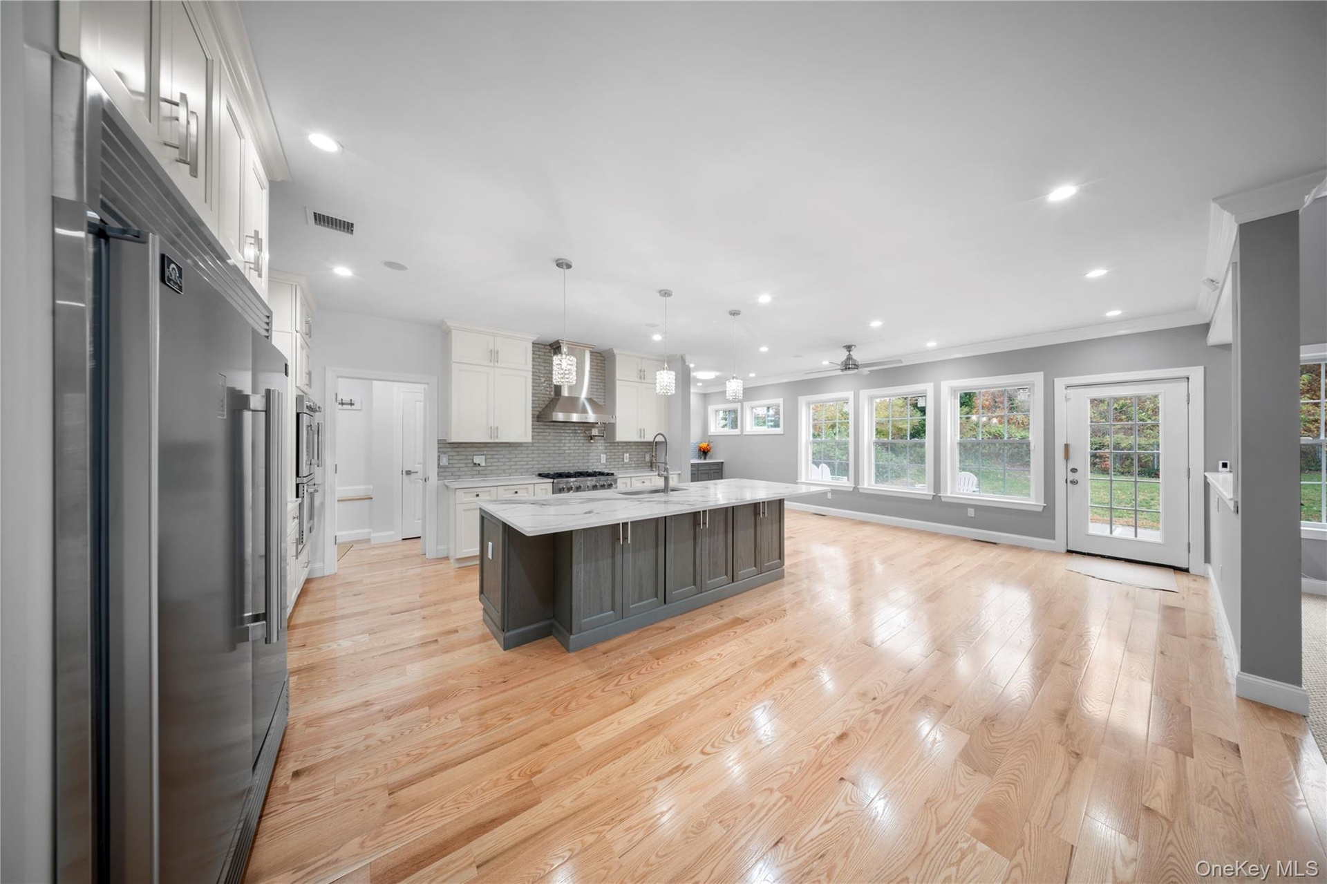 Kitchen featuring appliances with stainless steel finishes, white cabinets, tasteful backsplash, hanging light fixtures, and light wood-type flooring