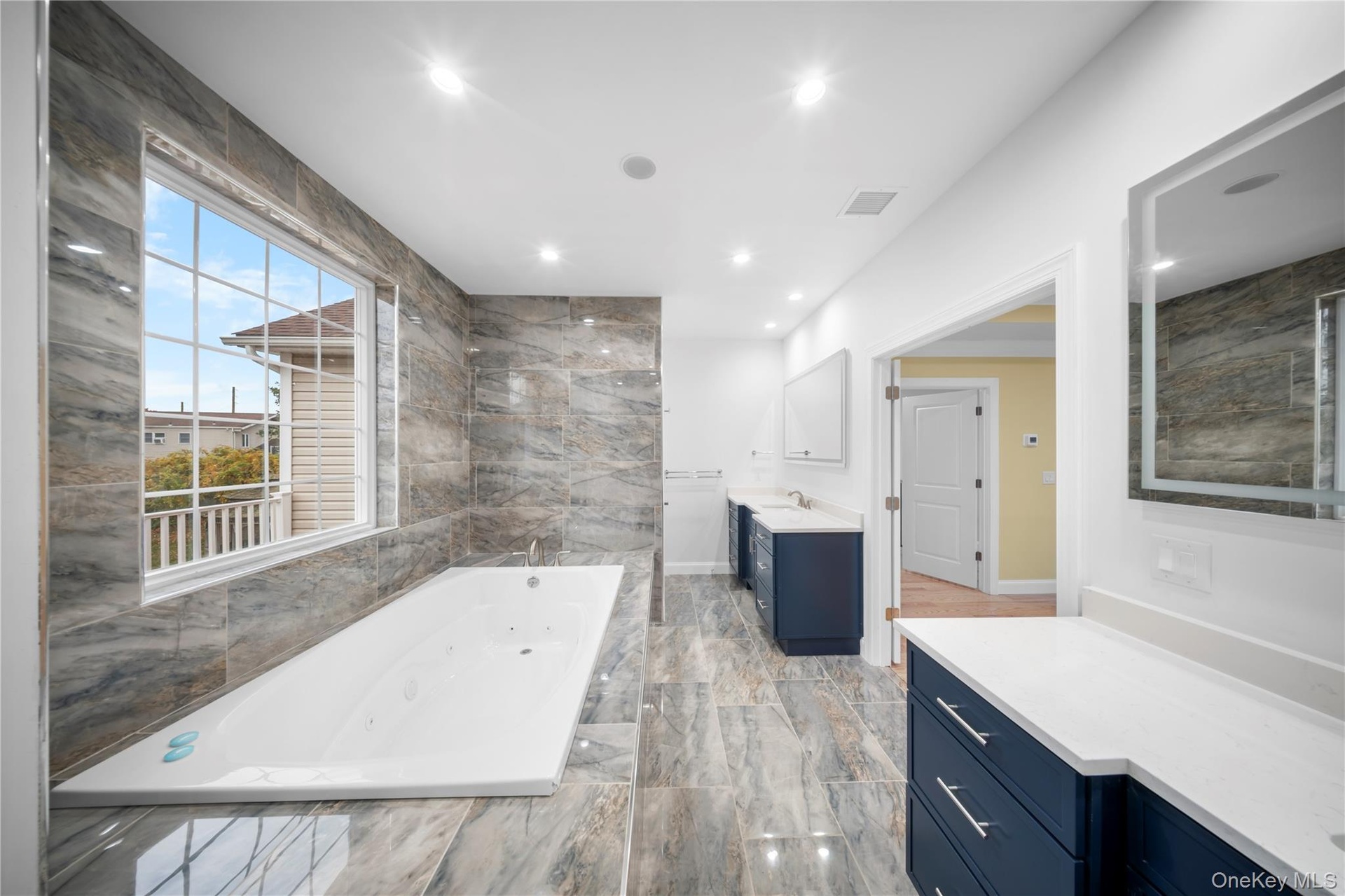 Bathroom with two vanities, a tub with jets, and recessed lighting