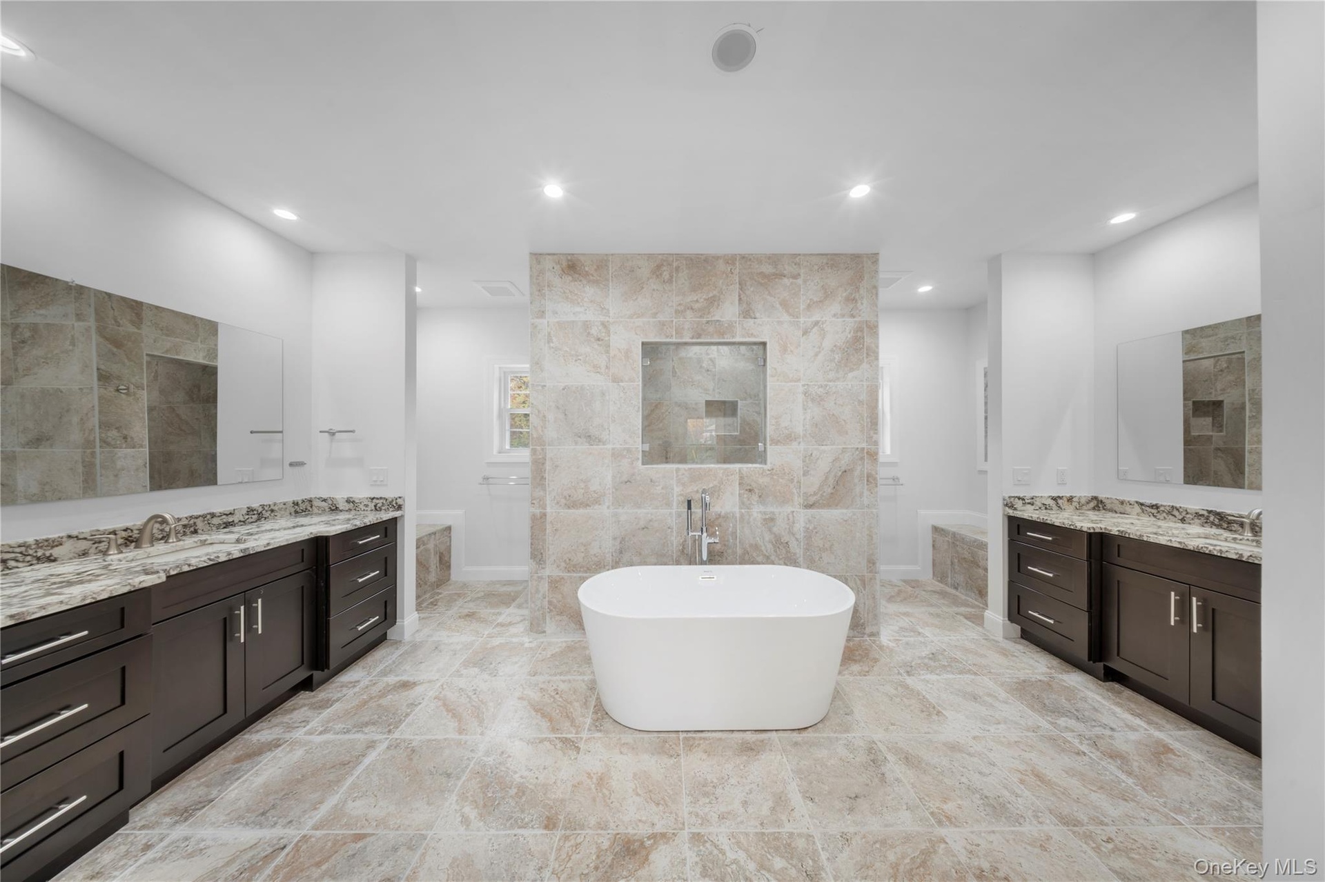 Bathroom with a freestanding tub, two vanities, recessed lighting, tile walls, and walk in shower