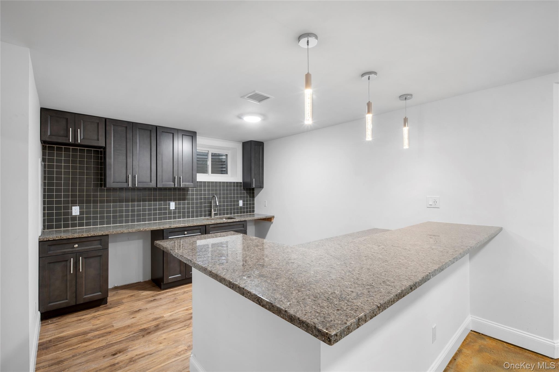 Kitchen featuring a peninsula, tasteful backsplash, hanging light fixtures, light wood-style floors, and light stone counters