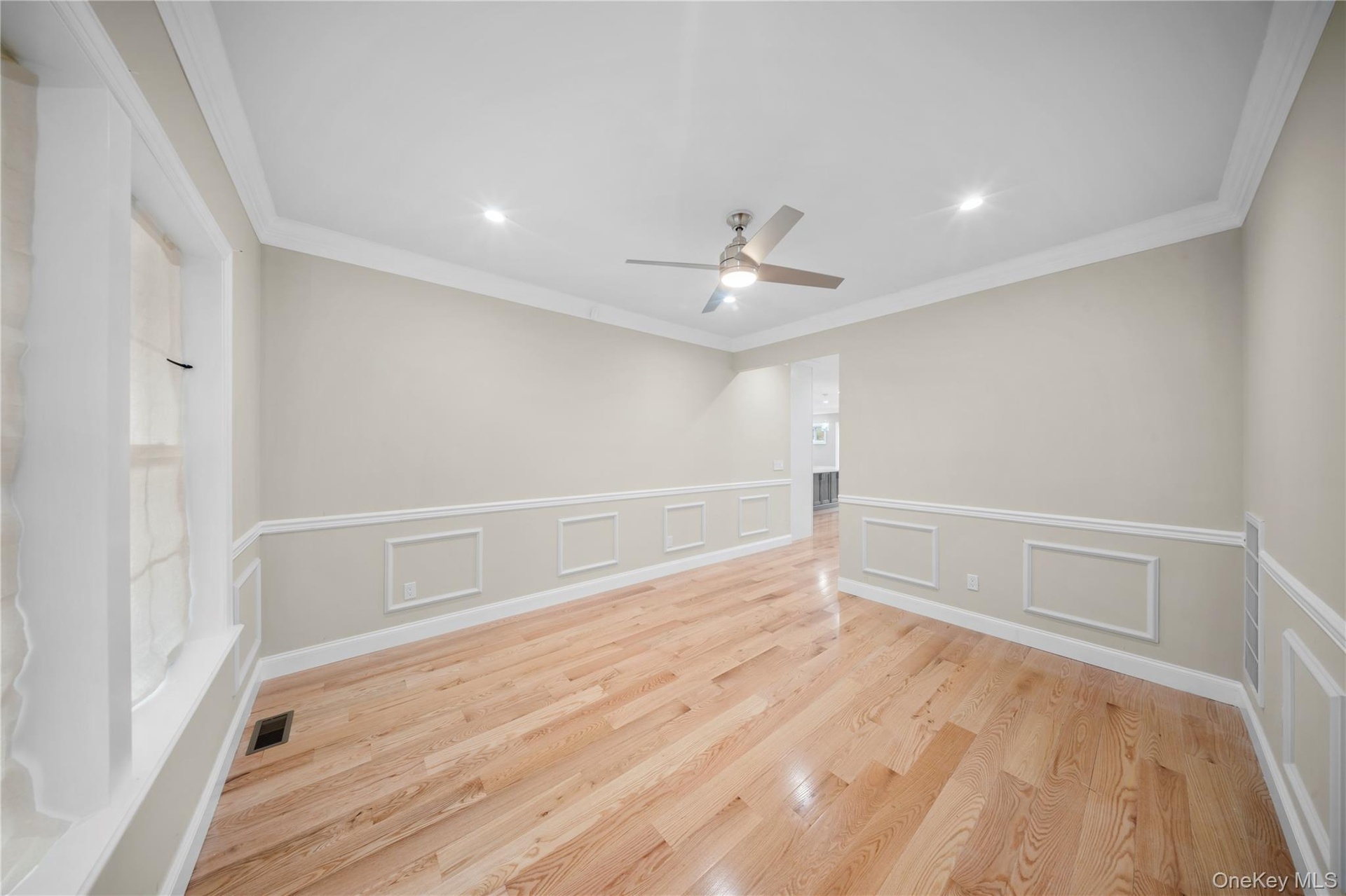 Empty room featuring a decorative wall, light wood finished floors, ornamental molding, recessed lighting, and wainscoting