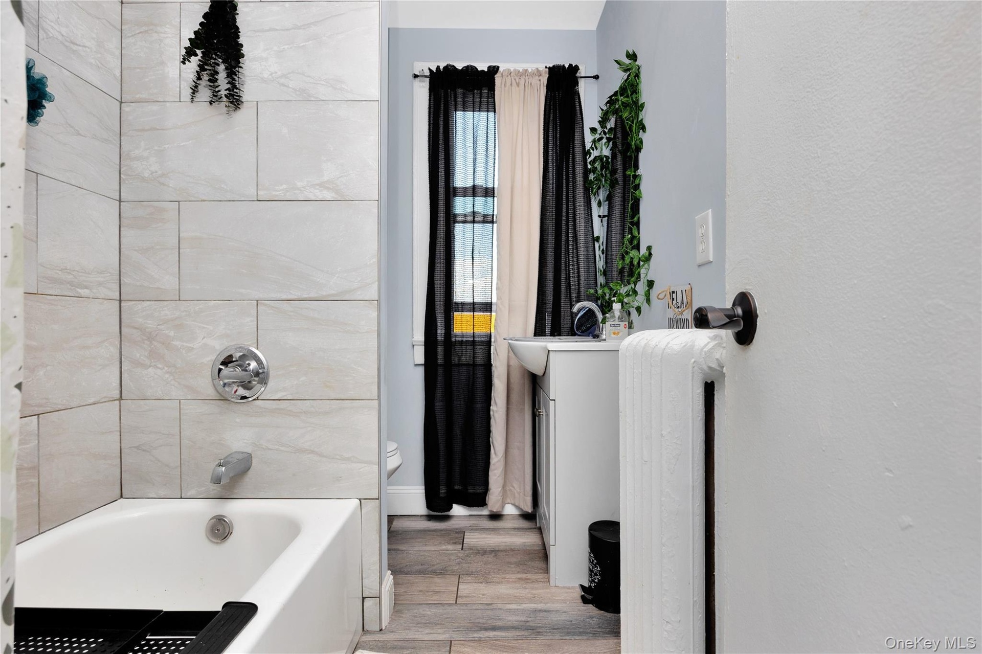 Bathroom with wood finished floors, shower / tub combination, radiator heating unit, and vanity