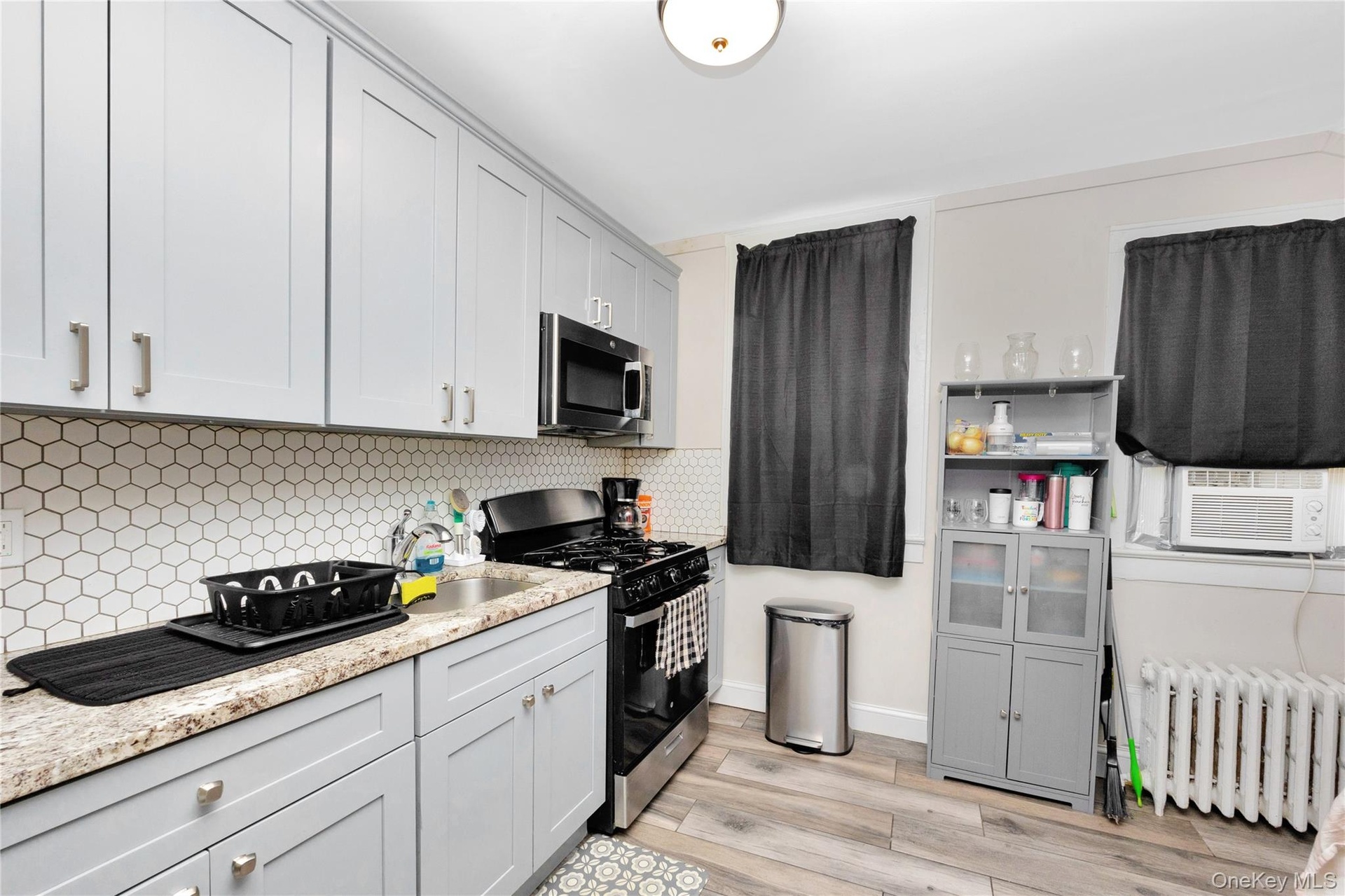 Kitchen featuring stainless steel appliances, radiator heating unit, cooling unit, light wood-style floors, and backsplash