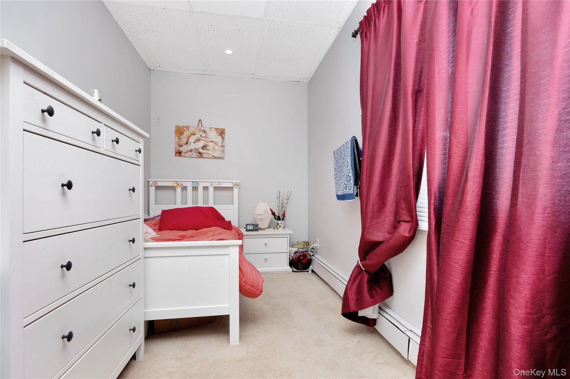 Bedroom featuring baseboard heating, light carpet, and a paneled ceiling