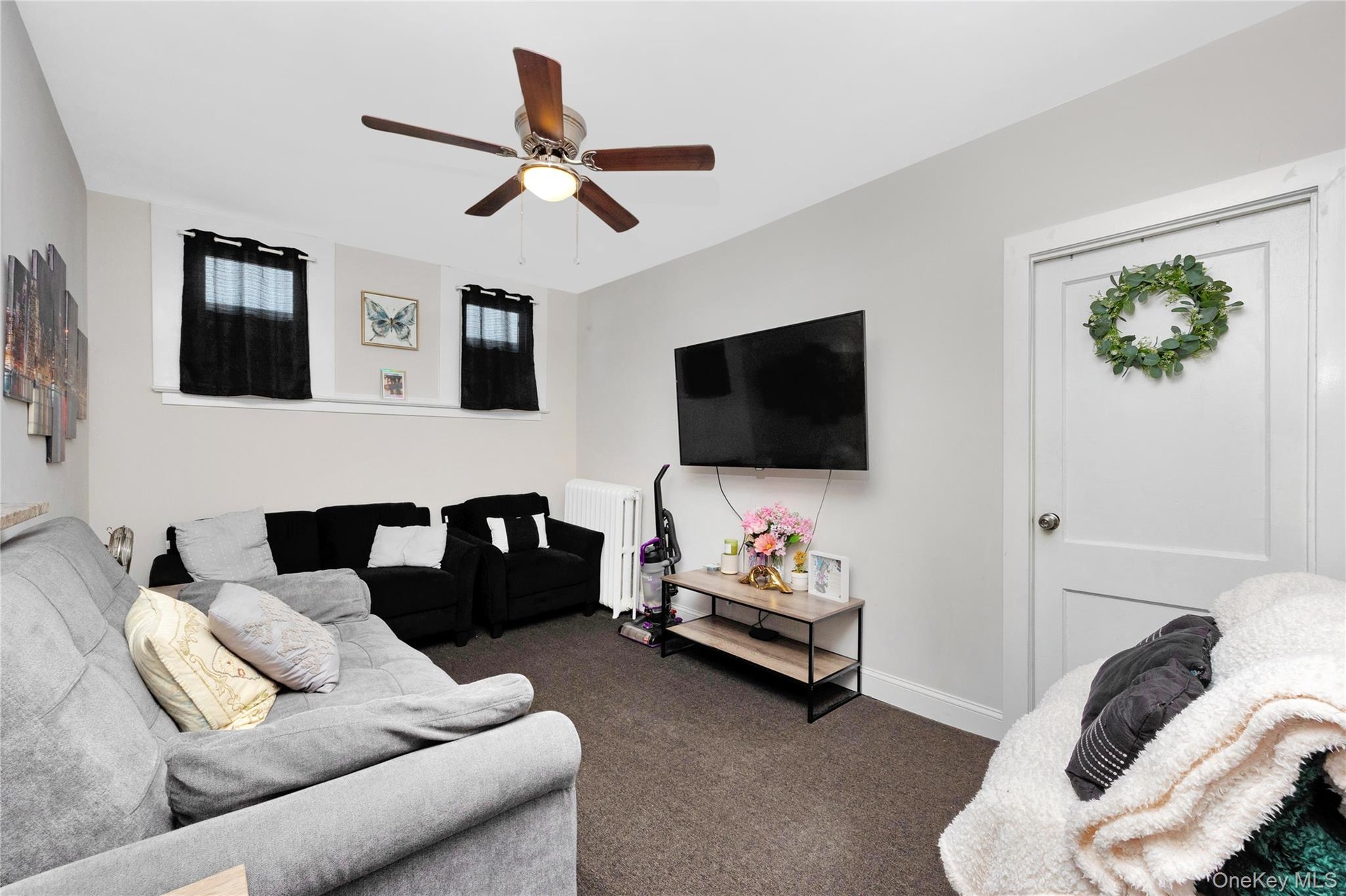 Living room featuring radiator heating unit, carpet flooring, and ceiling fan