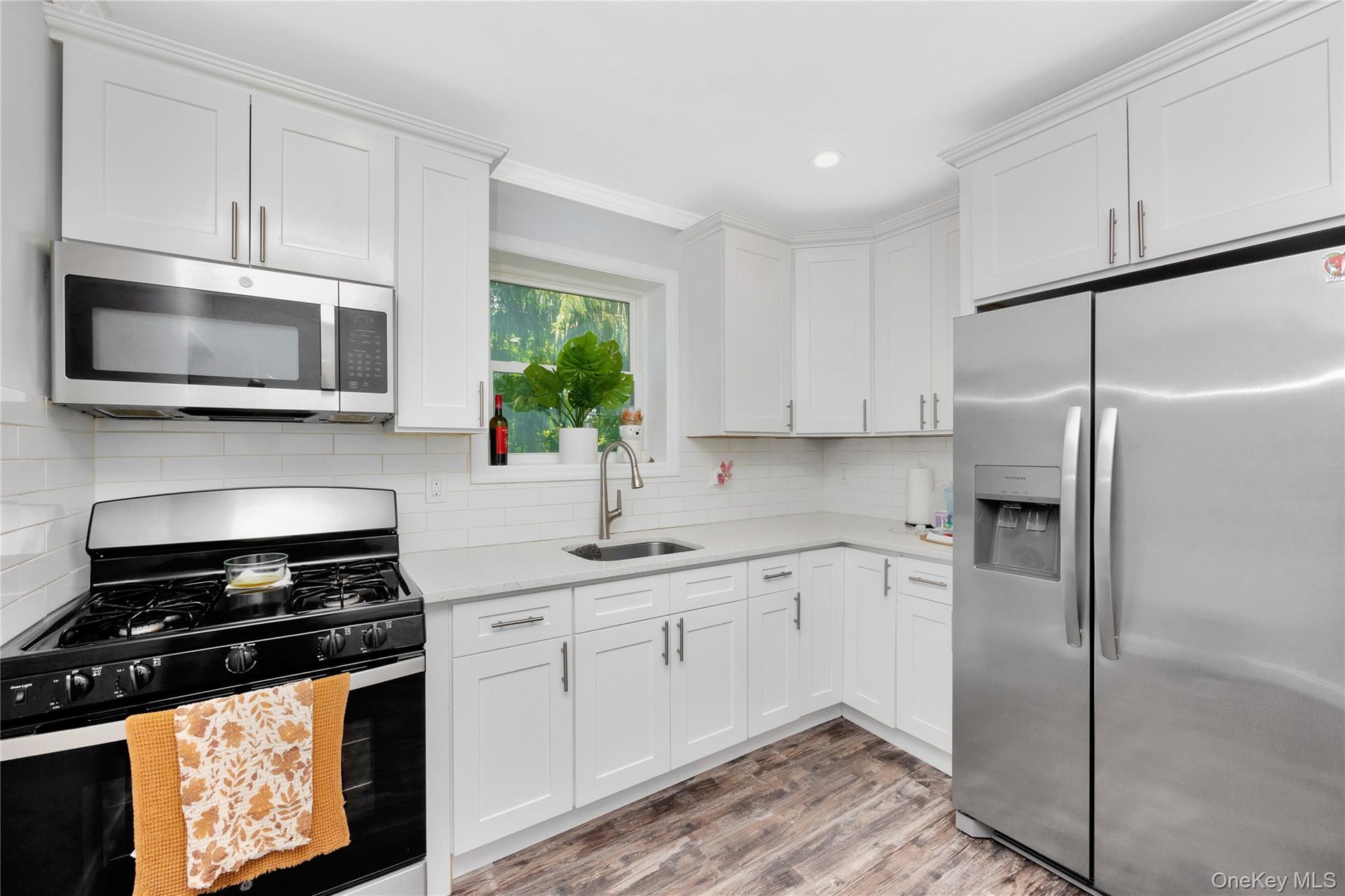 Kitchen featuring appliances with stainless steel finishes, light countertops, white cabinetry, light wood-style flooring, and decorative backsplash