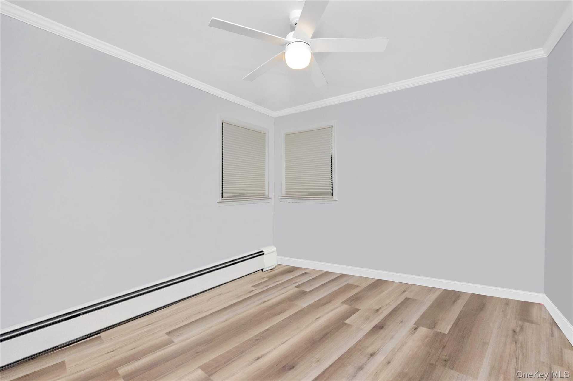 Empty room featuring a baseboard radiator, light wood-style floors, crown molding, and ceiling fan