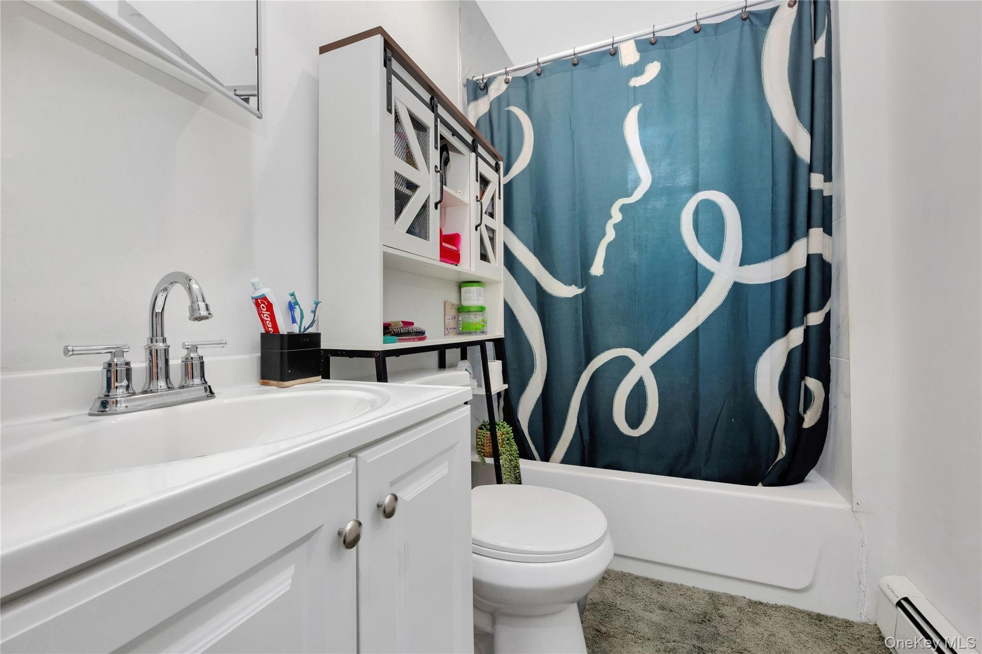 Full bath with a baseboard radiator, vanity, and shower / bath combo with shower curtain