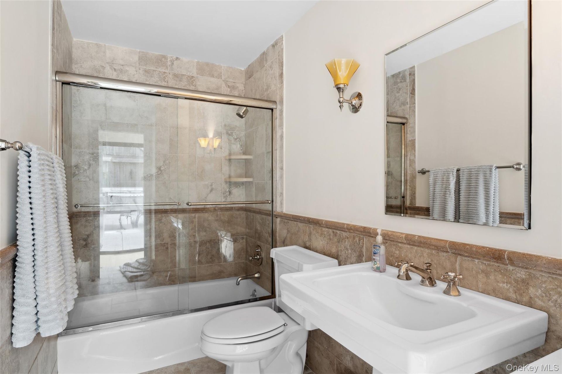 Bathroom with enclosed tub / shower combo, tile walls, and a wainscoted wall