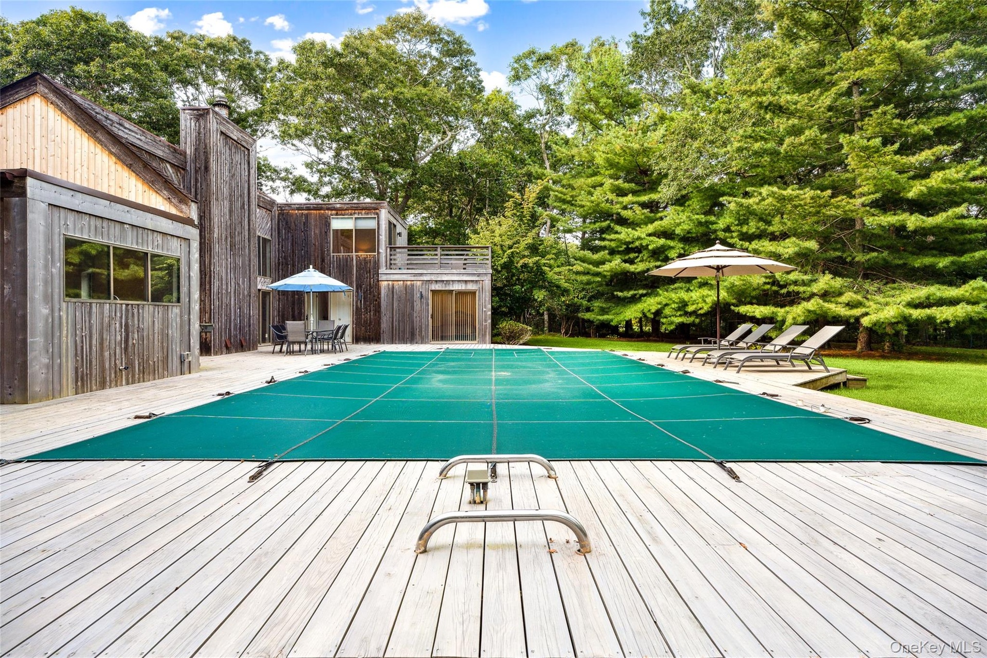 View of pool featuring a covered pool, outdoor dining space, view of wooded area, a deck, and a patio area
