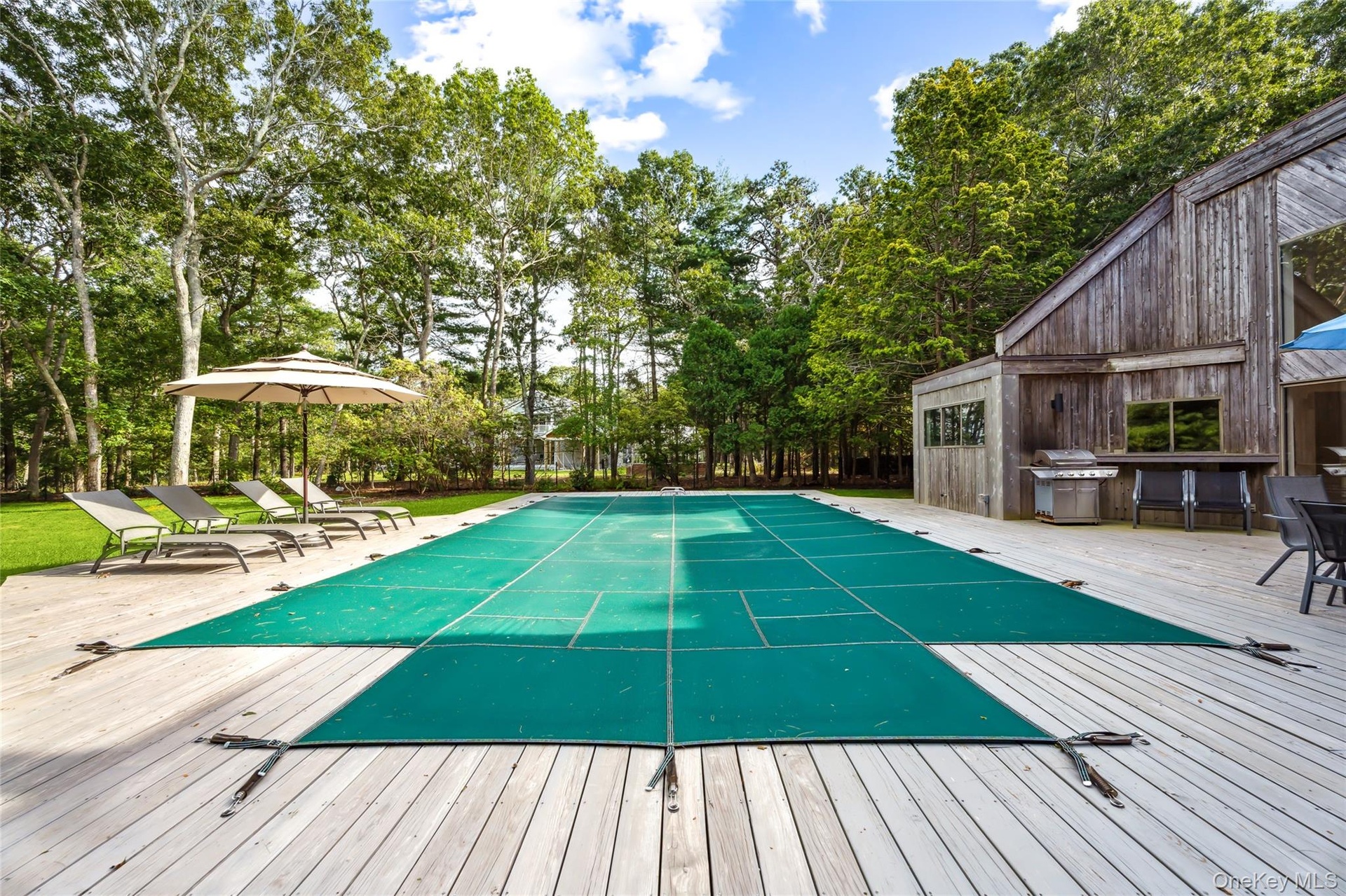 View of swimming pool featuring view of wooded area, a covered pool, a wooden deck, and grilling area