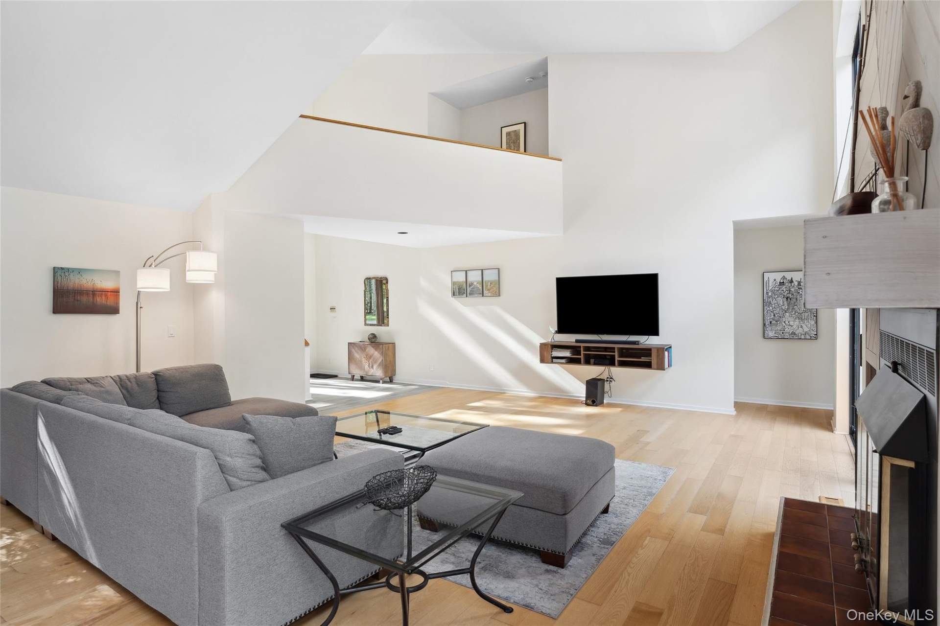 Living room featuring a tiled fireplace, light wood-style floors, and a towering ceiling