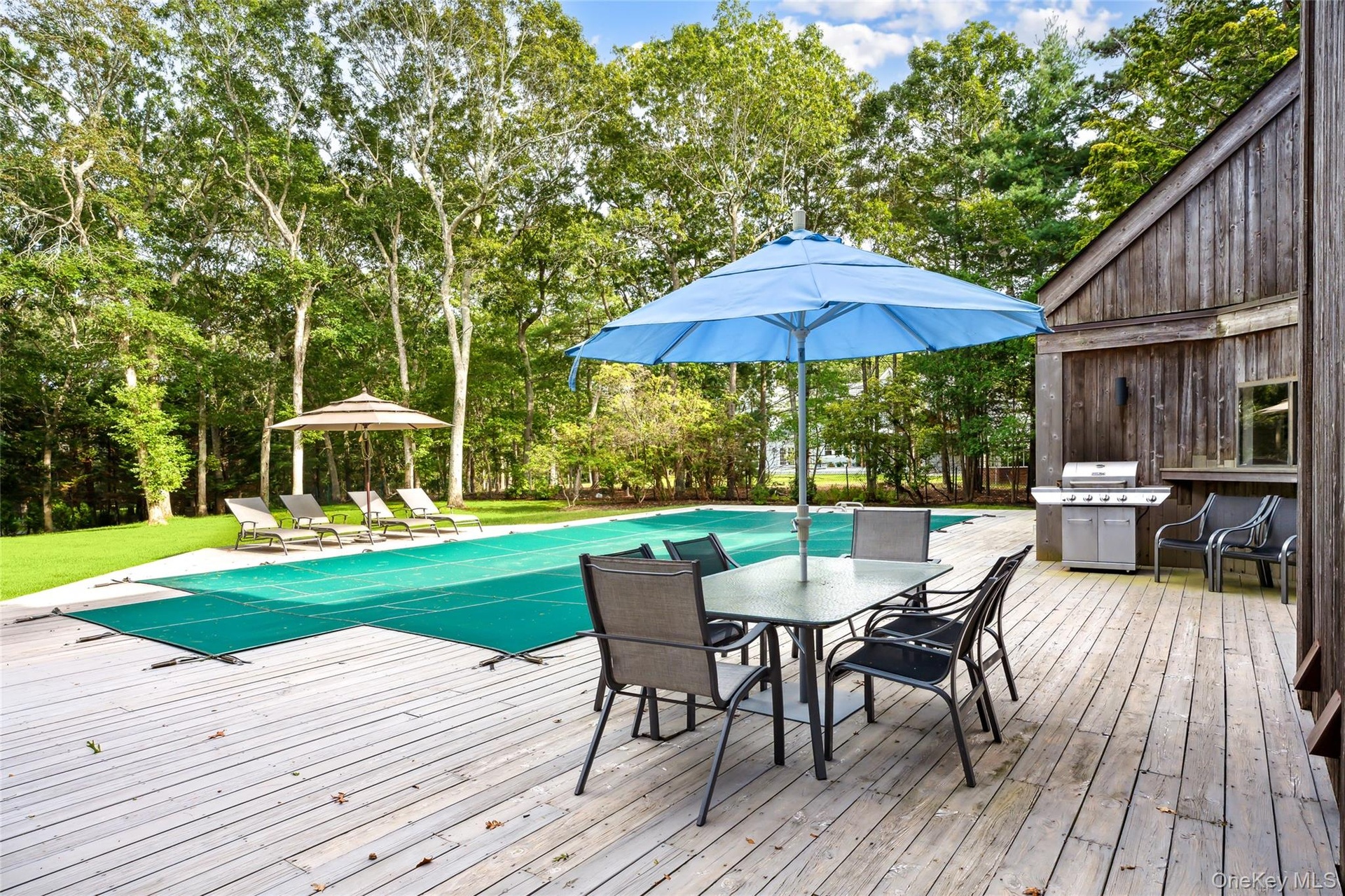 Wooden deck with a covered pool, outdoor dining area, a grill, and view of wooded area
