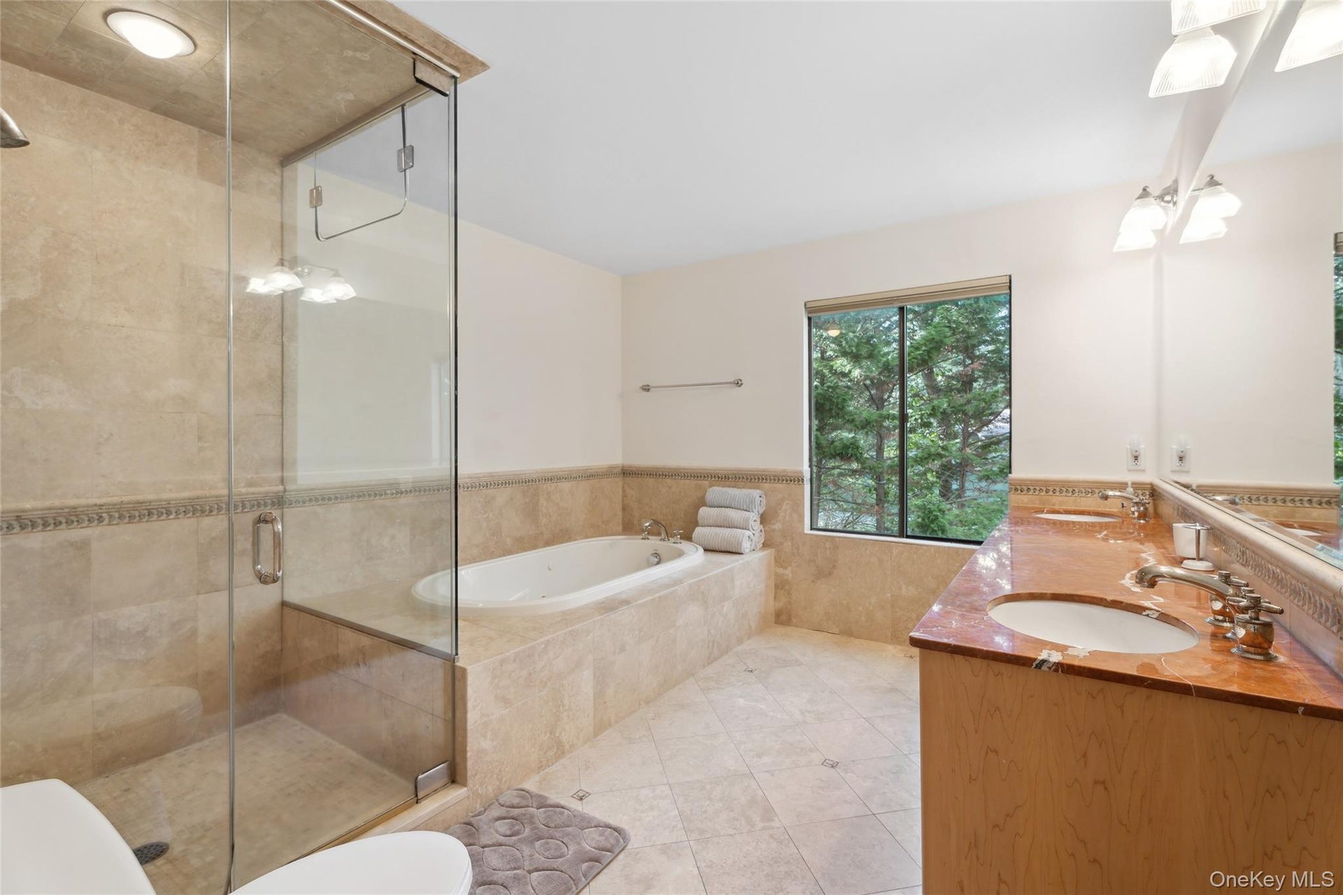 Full bathroom featuring wainscoting, double vanity, a stall shower, a bath, and tile walls