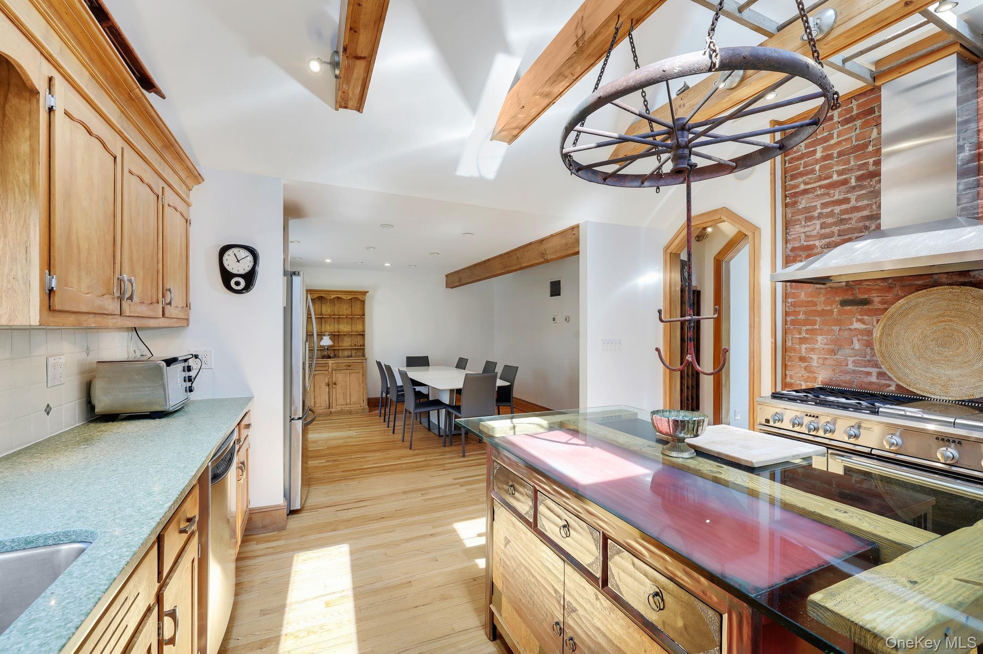 Kitchen featuring a Wolf gas cooktop and electric oven,  exposed brick backsplash, and a custom made central island with a glass countertop.