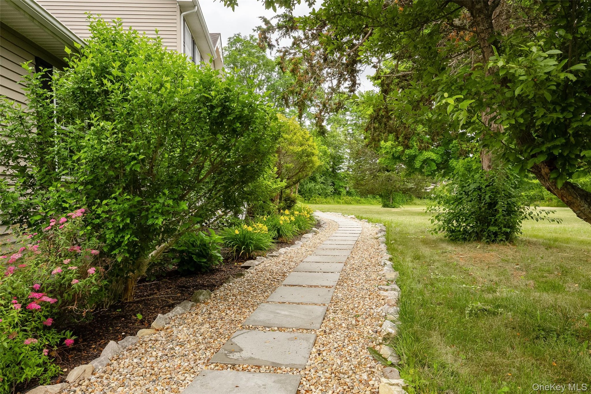 Curved stepping stone pathway bordered by gravel, leading through a spacious lawn