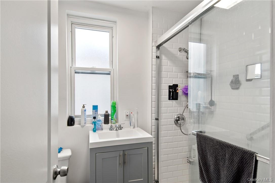 Bathroom featuring a single window, a vanity with a white countertop and gray cabinetry, and a shower enclosure with white subway tile