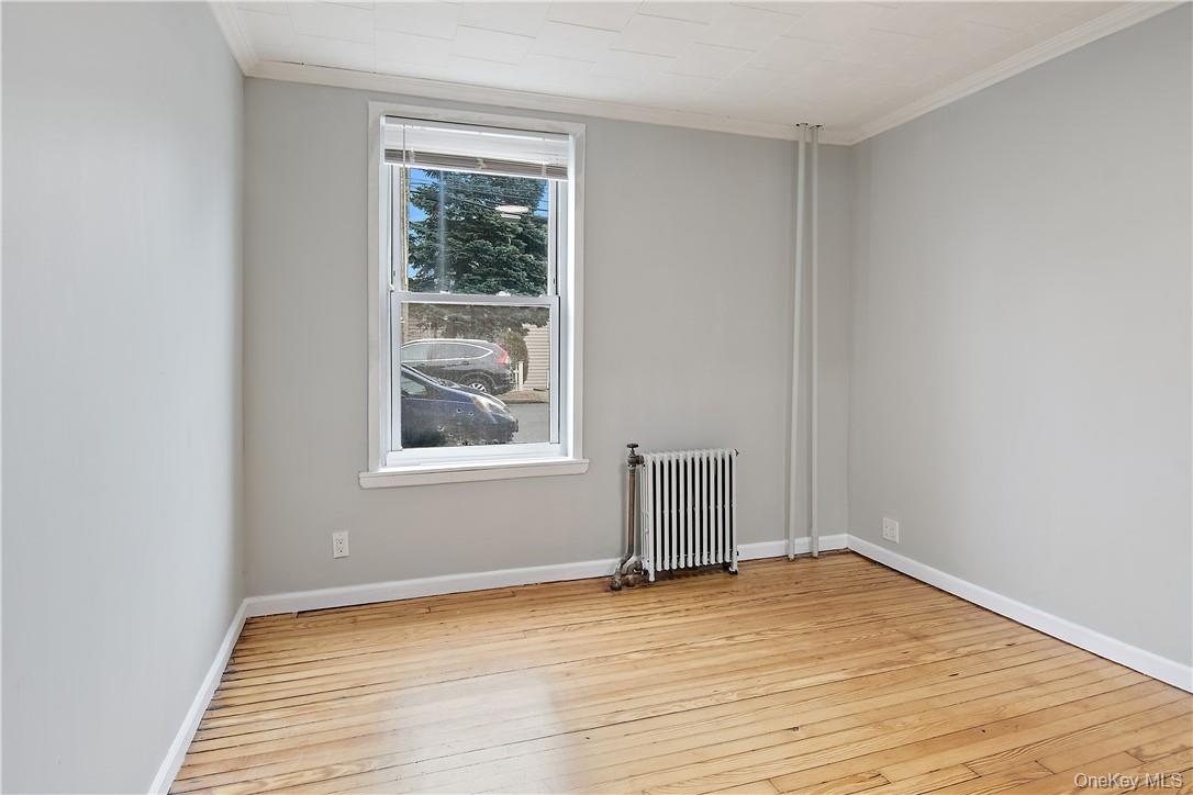 Room featuring wood flooring, neutral wall paint, a double-hung window, and a radiator heating unit