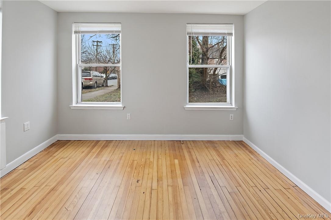 Room featuring natural wood flooring, two double-hung windows with blinds, light gray wall paint, and white baseboards