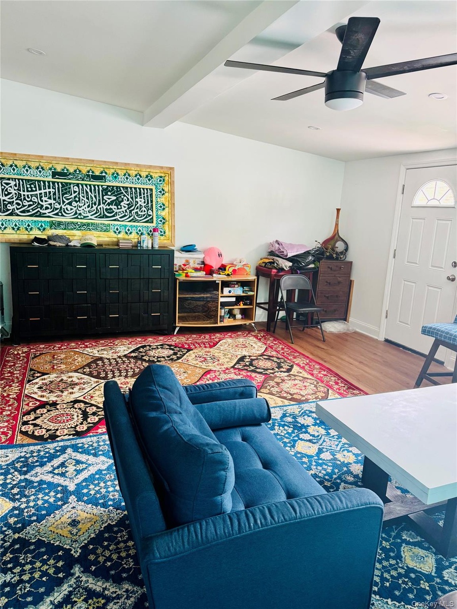 Living area featuring wood finished floors, ceiling fan, and beamed ceiling