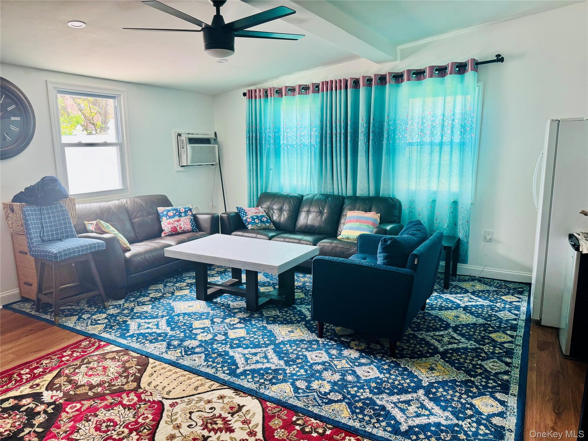 Living area featuring wood finished floors, ceiling fan, an AC wall unit, baseboards, and beam ceiling