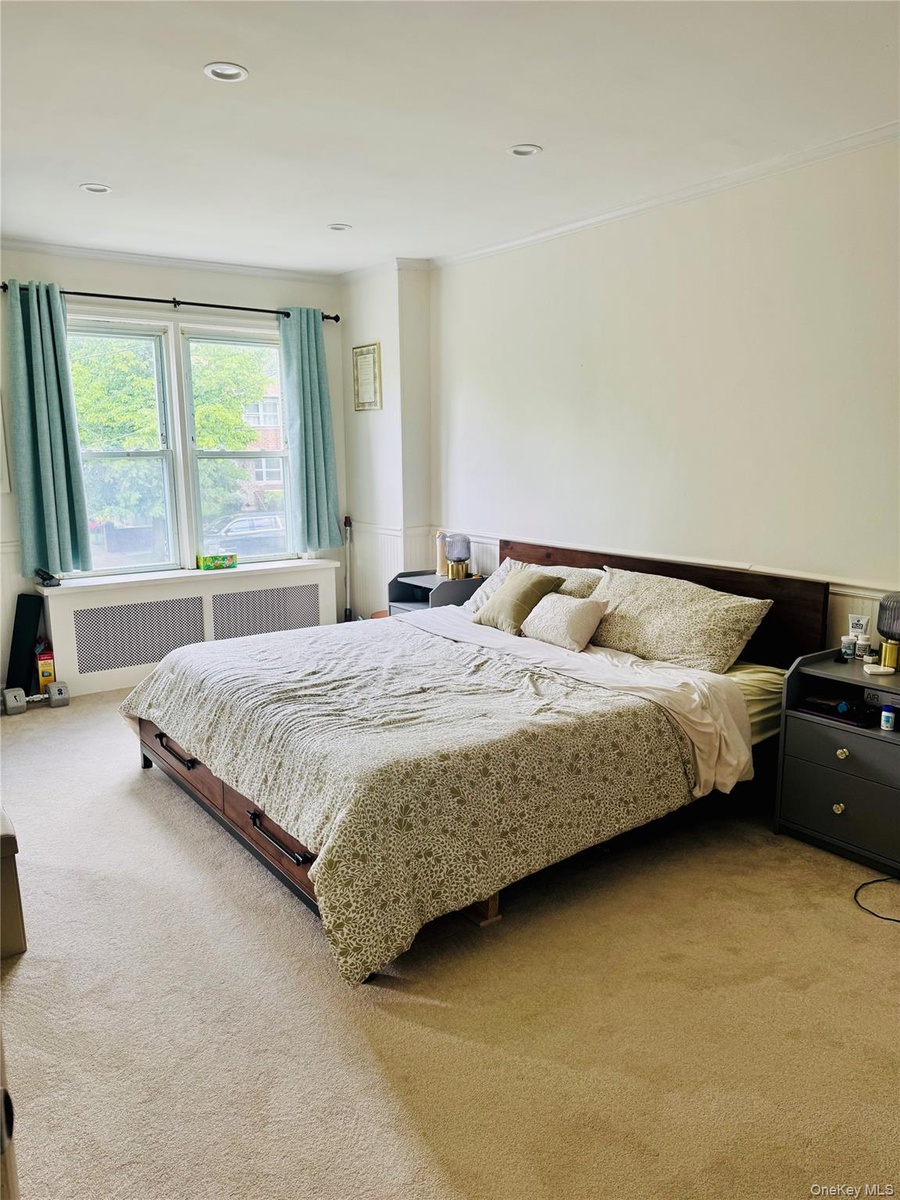 Bedroom with light carpet, radiator heating unit, and ornamental molding