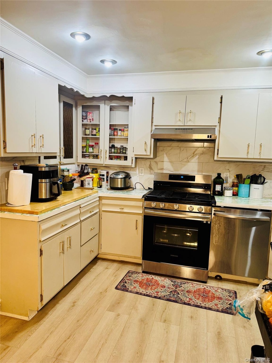 Kitchen featuring appliances with stainless steel finishes, light countertops, light wood-style floors, under cabinet range hood, and decorative backs