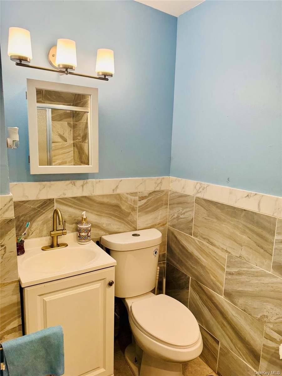 Full bath with tile walls, vanity, toilet, an enclosed shower, and a wainscoted wall