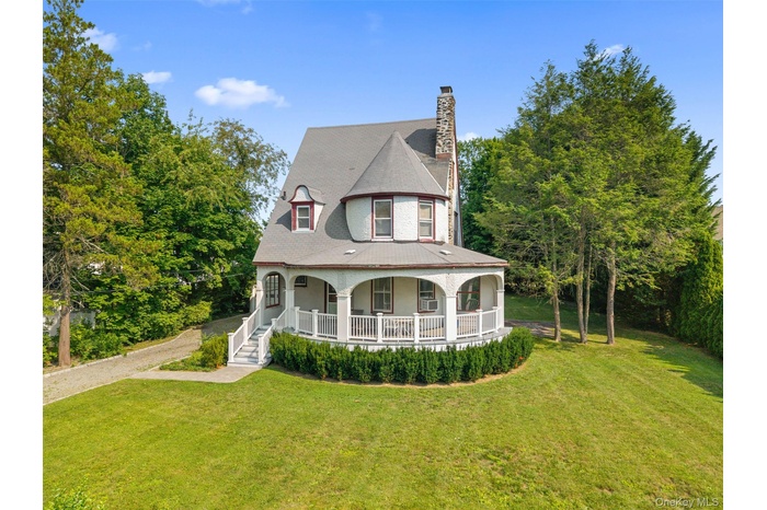 Charming stucco exterior featuring a prominent turret, stone chimney, dormer windows, and wraparound porch.
