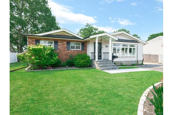 Exterior featuring a brick facade, white siding, a covered entry with black railings, a large bay window, and a stone walkway