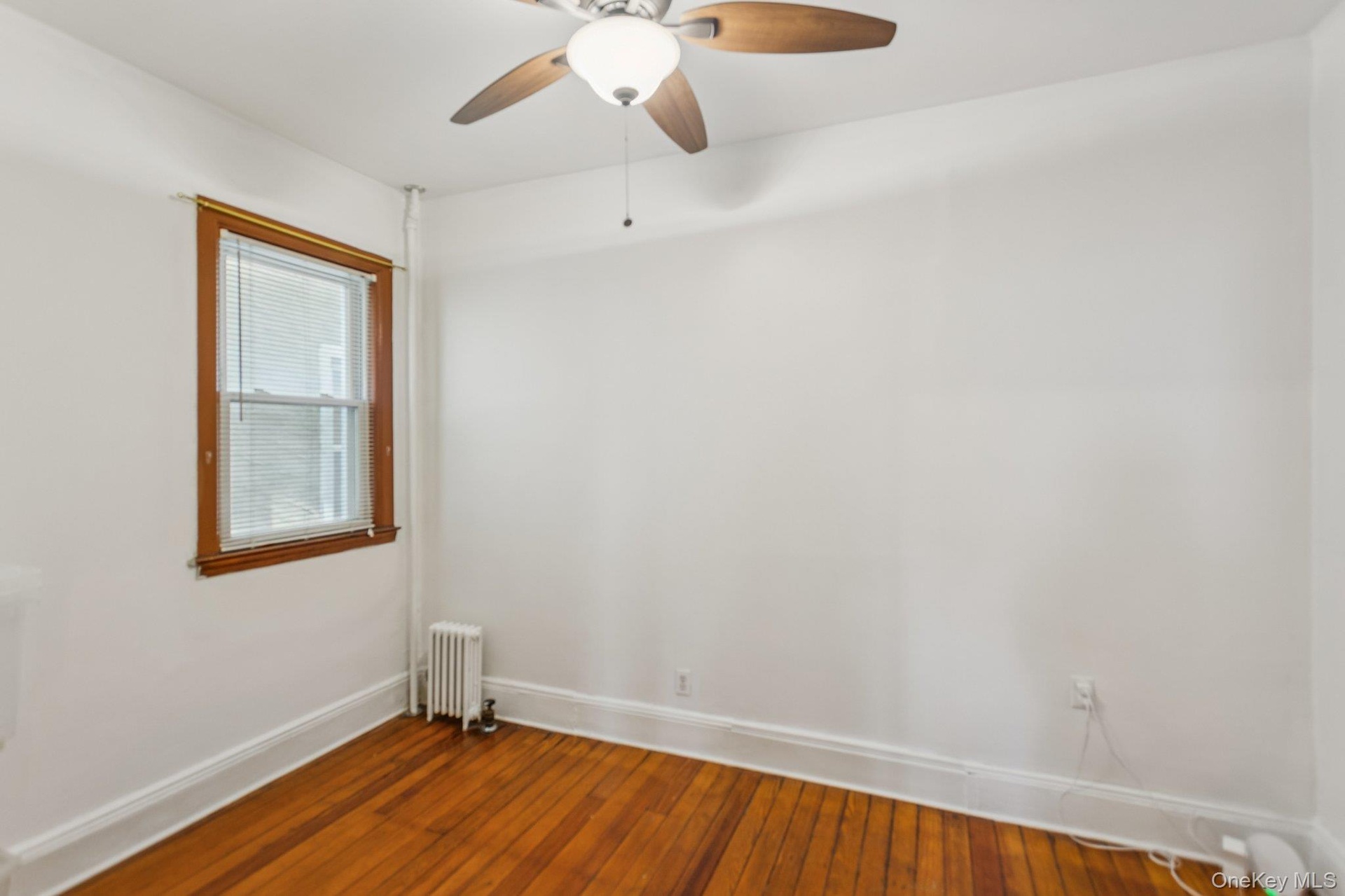 Spare room with radiator heating unit, dark wood finished floors, and ceiling fan