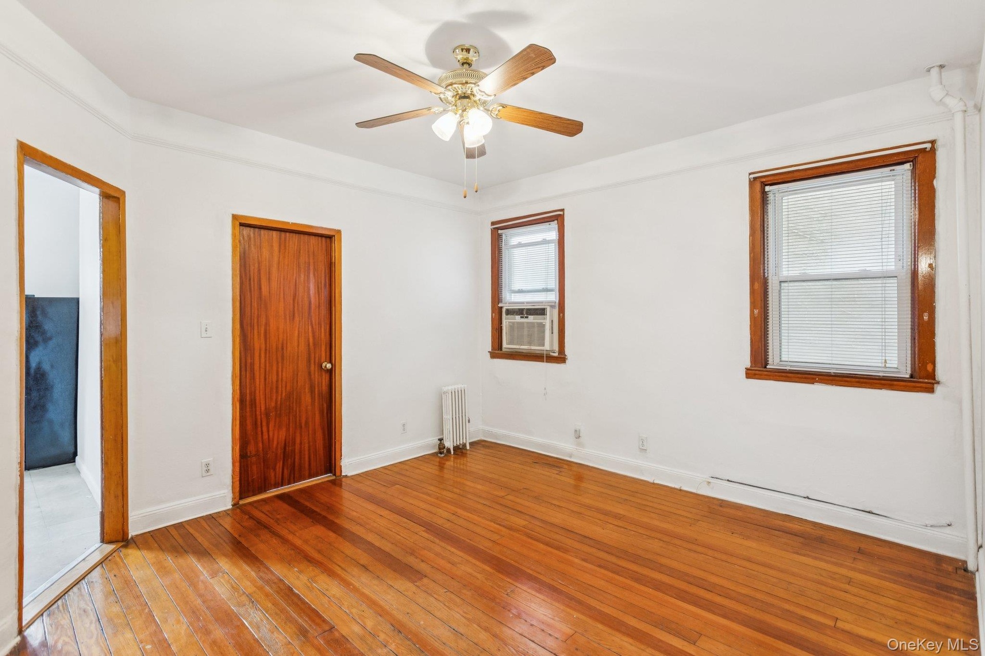 Unfurnished bedroom with radiator, light wood finished floors, cooling unit, and a ceiling fan
