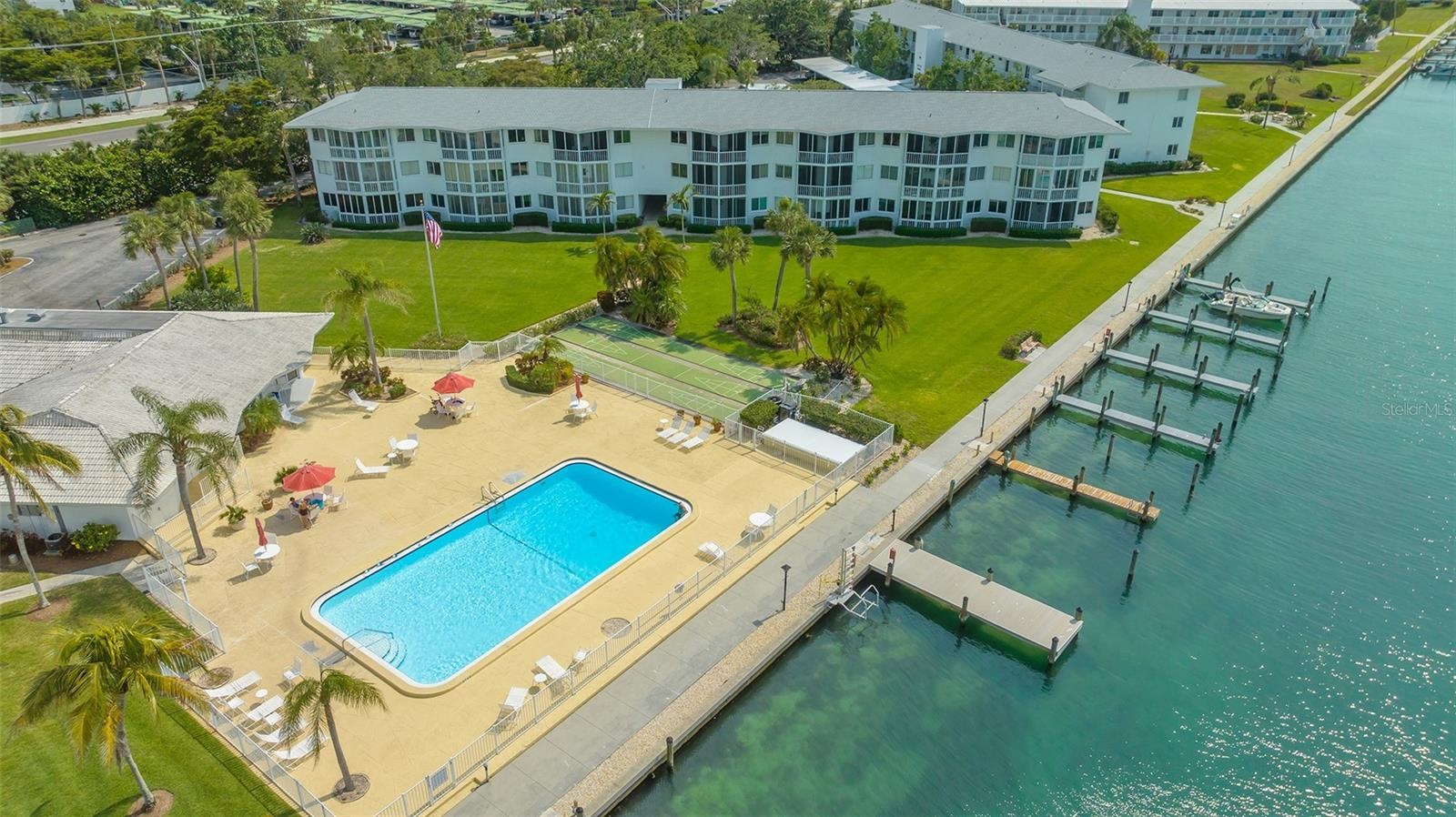 This aerial view highlights the expansive pool deck, clubhouse, deck shuffleboard courts and boat docks