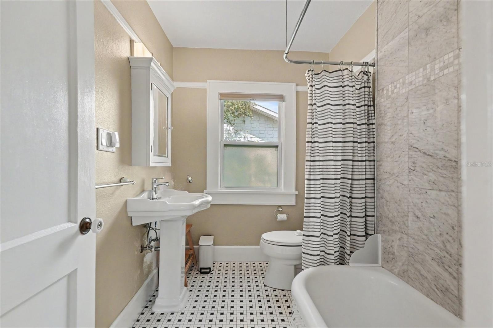 The full bathroom blends vintage character with thoughtful updates, including classic tilework, a pedestal sink, and a tub/shower combination.