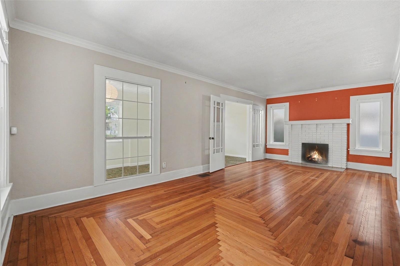 Sunlight, original wood floors, and a brick fireplace create a living room that feels warm, inviting, and unmistakably historic.