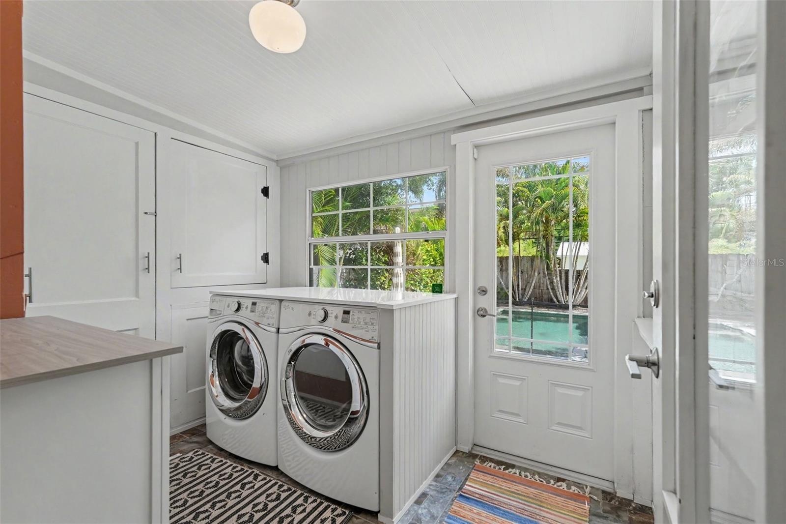 A bright and functional laundry room offers generous built-in storage, full-size washer and dryer space, and direct access to the pool and backyard.
