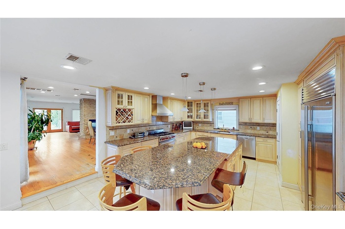 Spacious kitchen featuring an expansive island with a stone countertop, light wood-finish cabinetry, stainless steel appliances, and recessed lighting