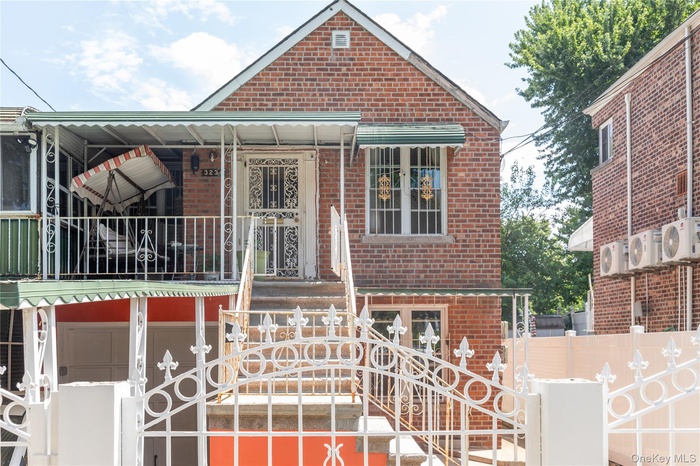 Brick facade residence featuring a covered entry porch, an upper-level balcony with white railings, and a decorative security gate