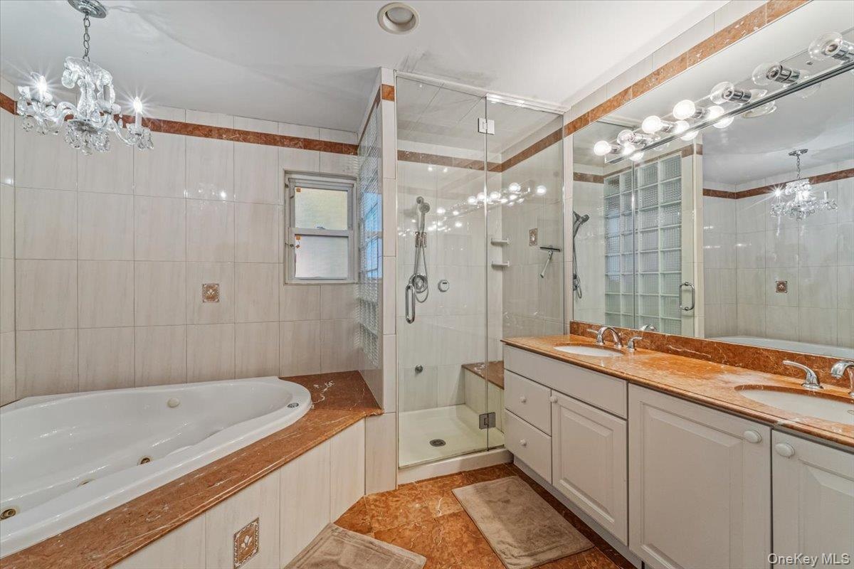 Bathroom featuring a built-in jetted tub, a glass-enclosed shower with a bench, and a dual-sink vanity with white cabinetry