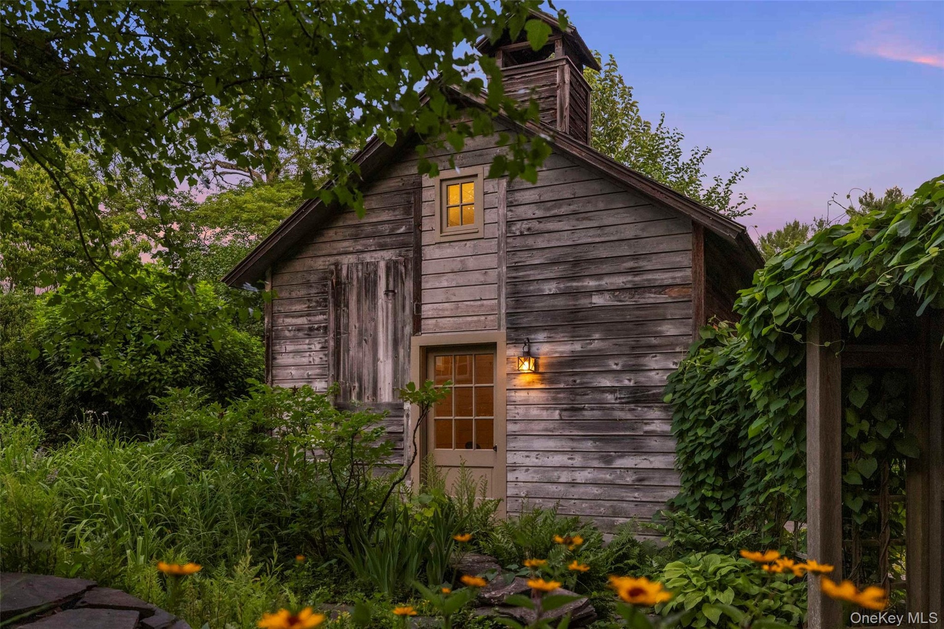 As evening falls, the wellness studio glows warmly amid mature gardens and lush landscaping